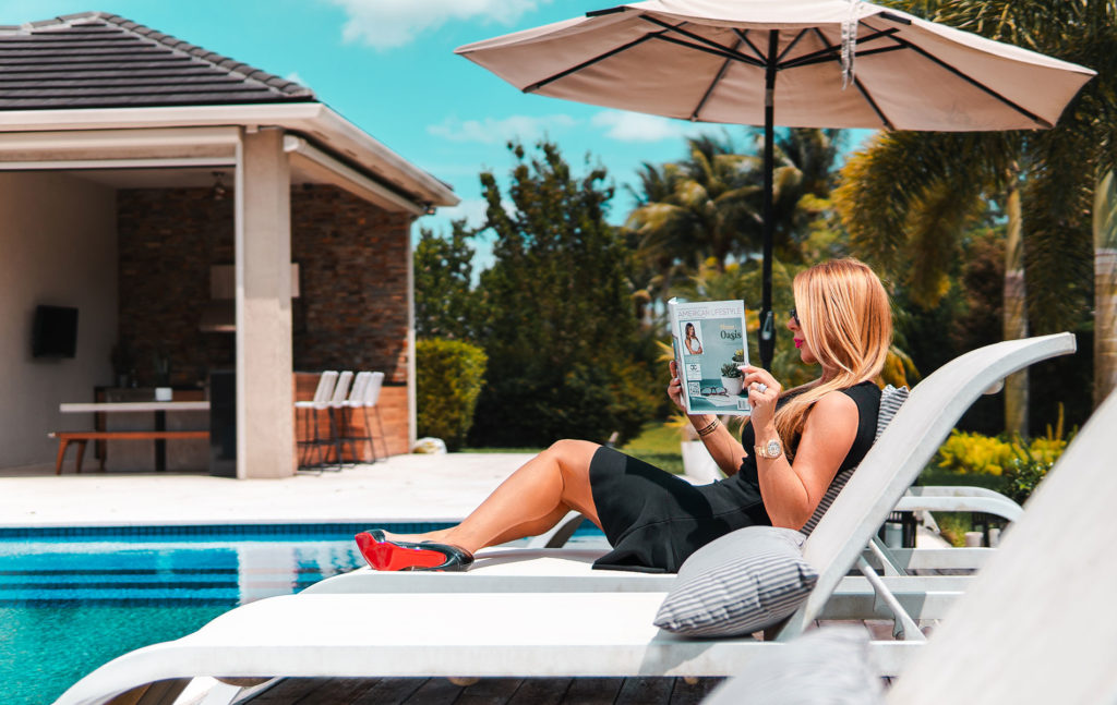 a women in a sun lounger beside a pool reading a real estate forecast 2021 in a luxury home at Fort Lauderdale FL